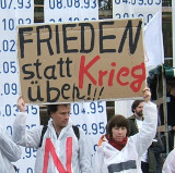 Ein Mann und eine Frau halten ein Schild hoch: Frieden statt Krieg üben